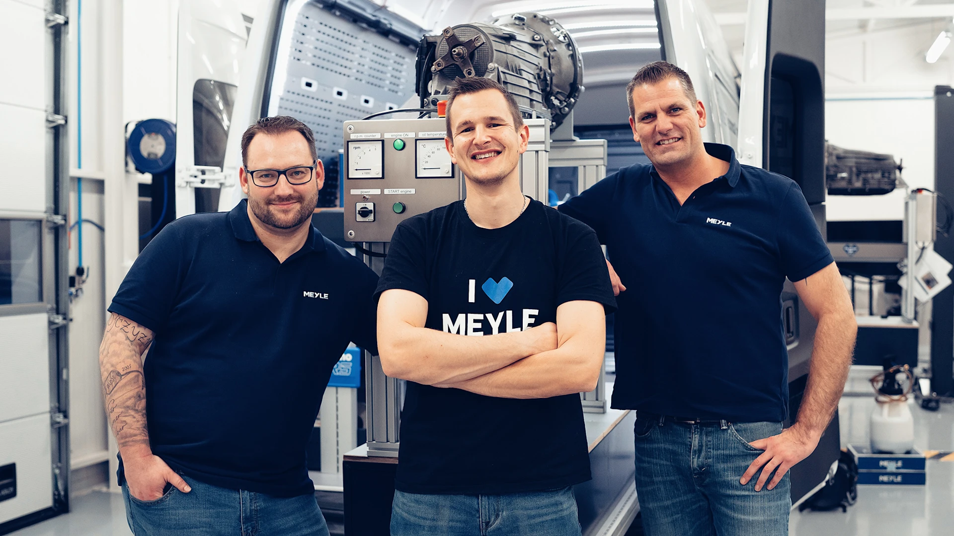 Drei MEYLE Trainer stehen vor ihrem Trainingstransporter und lächeln in die Kamera.