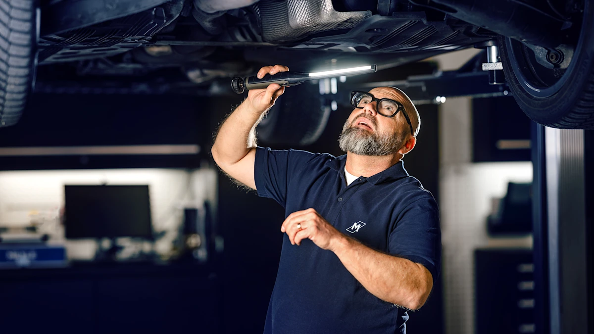 A person looks under a car with a flashlight. The car is on a lifting platform.