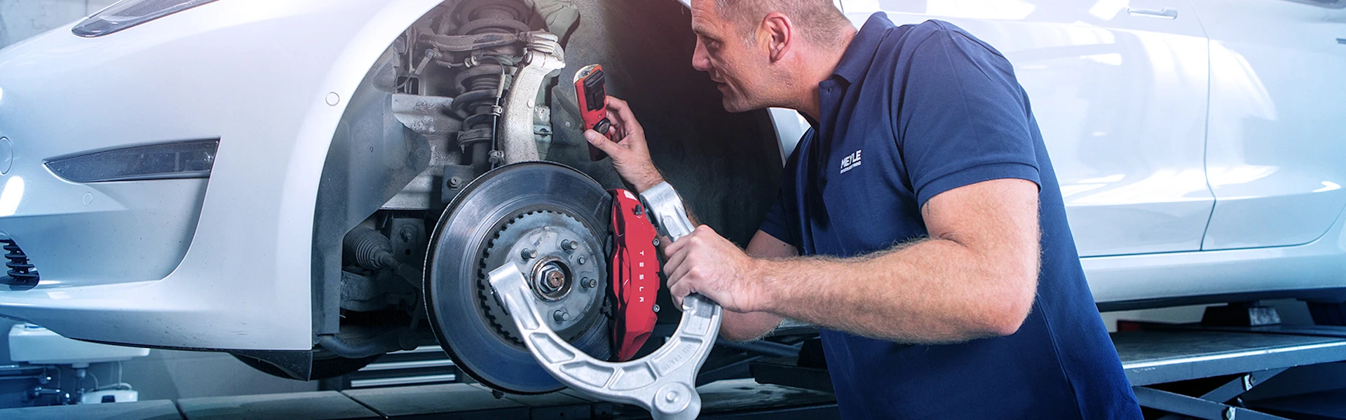 Mechanic looks at the suspension parts on the car with a lamp.