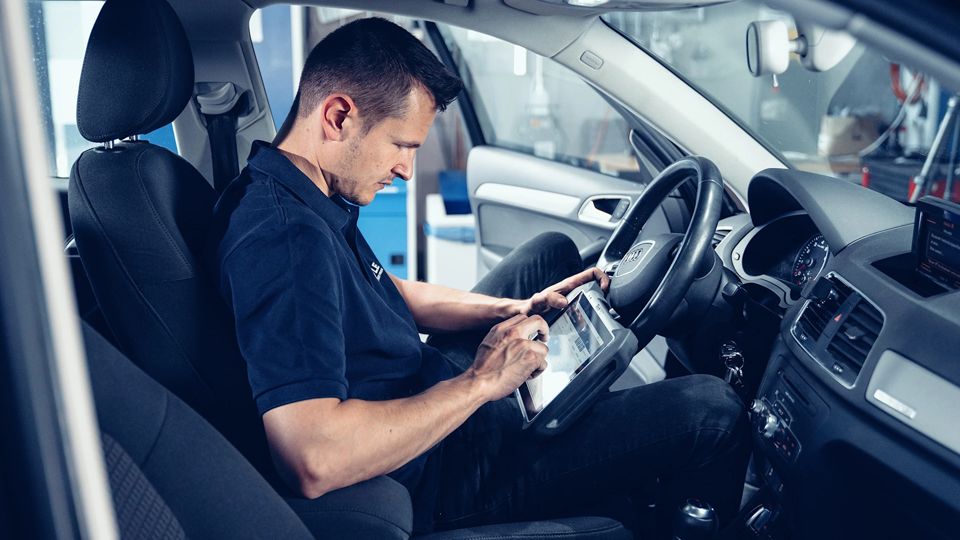 Person sits in a car in a workshop and checks data on a tablet.