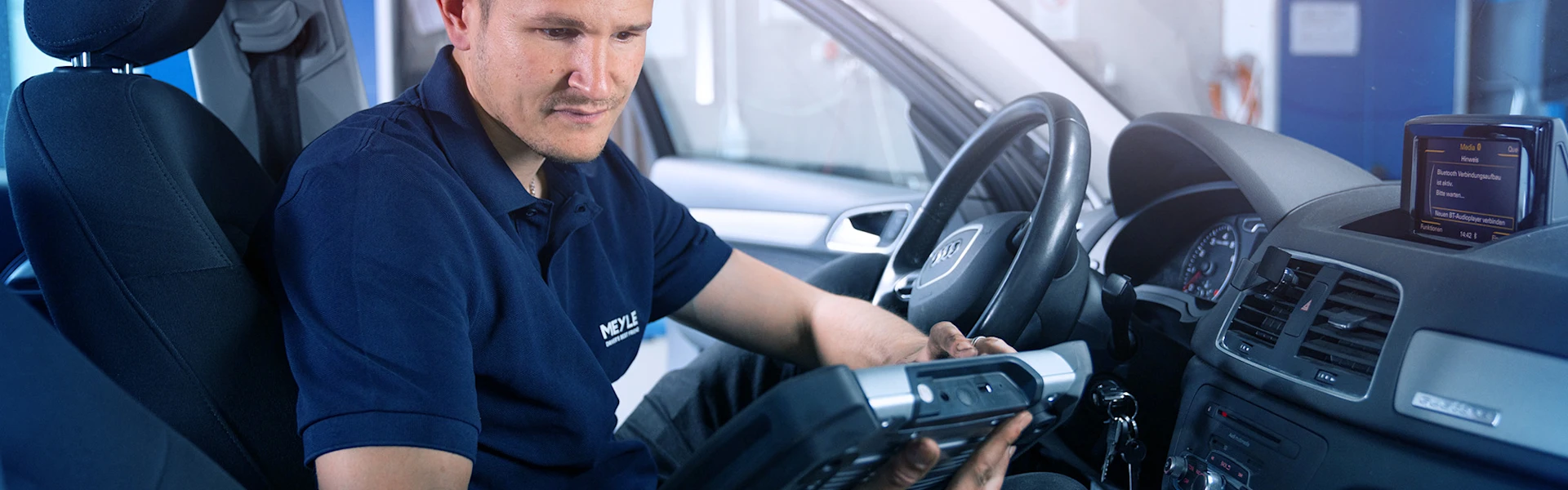 Mechaniker sitzt im Auto und liest Daten aus.